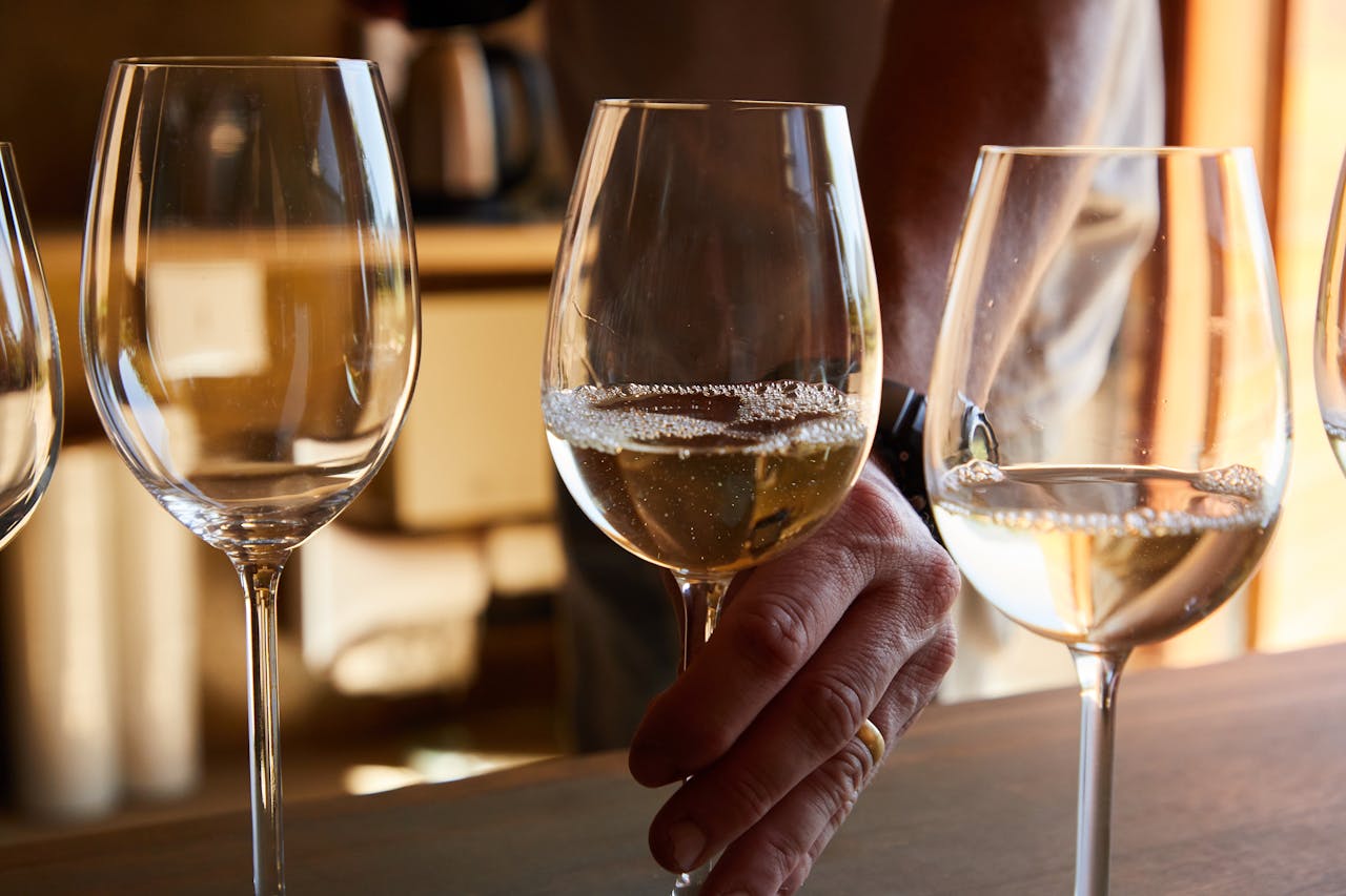 Close-up of a hand holding a wine glass filled with white wine, in a warm indoor setting.